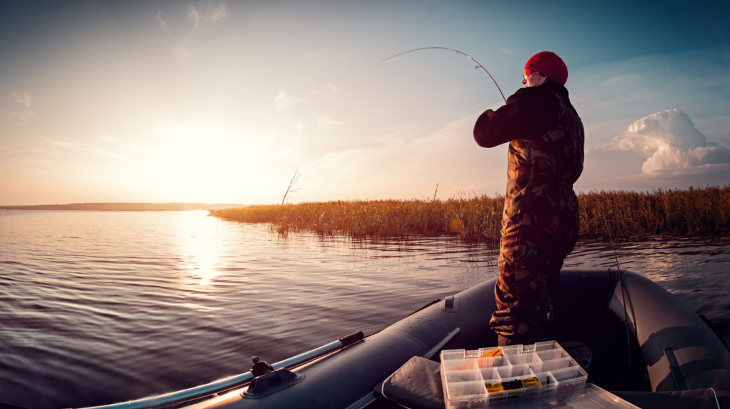 Man fishing from his fishing boat on the lake at sunset and annoyed from the people are stiill unaware of how to pass a fishing boat