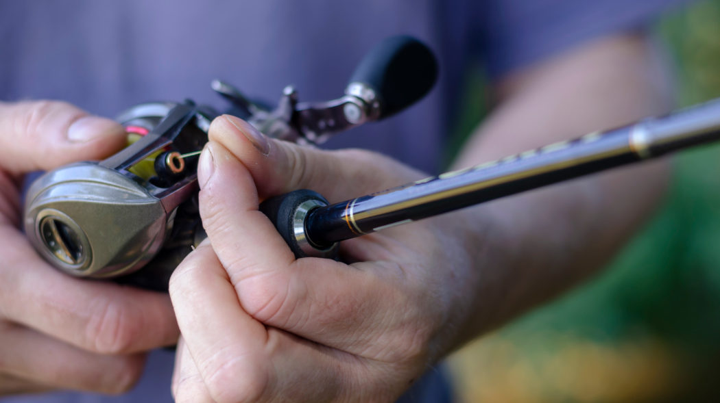 Close-up of a male hand with a fishing rod and a baitcasting reel. A Caucasian man sips a yellow braided line into the winding rings on a rod. Preparing for fishing. Selective focus.