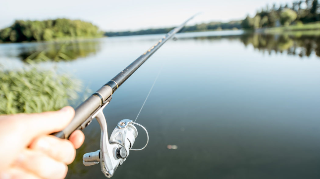 Fishing rod and fishing reel on the beautiful lake background during the morning light