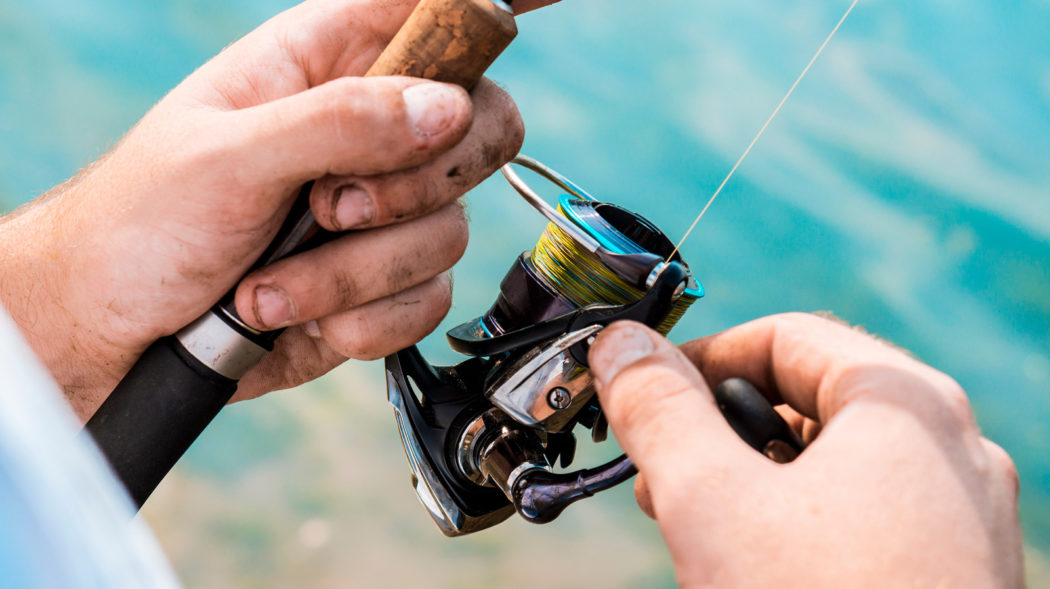 Spinning reel in the hands of a fisherman. Close-up.