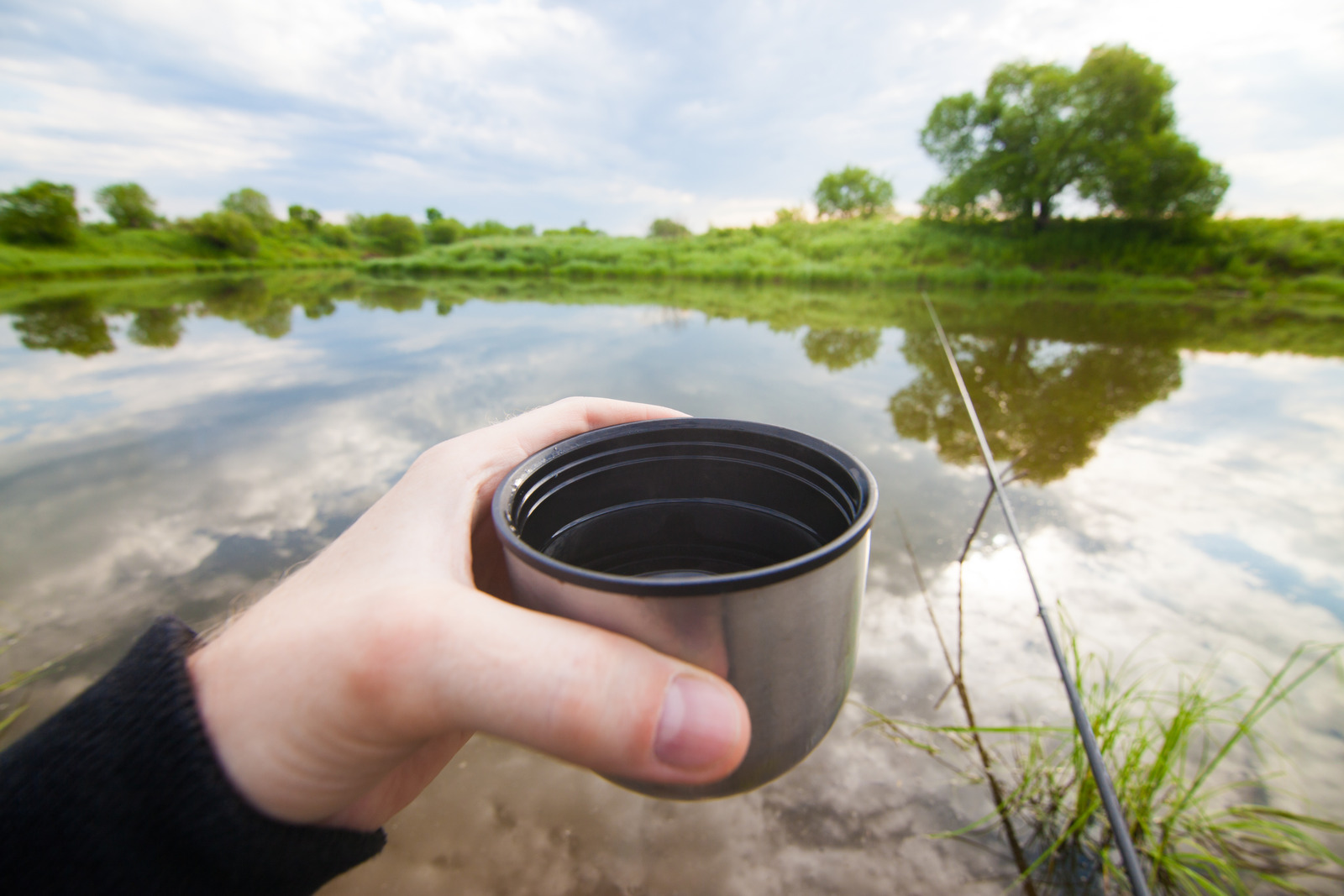 Fisherman is going to drink tea from thermos during fishing