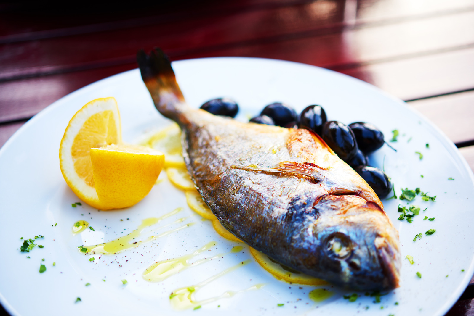 cooked fish - bream near lemon and black olives on plate.