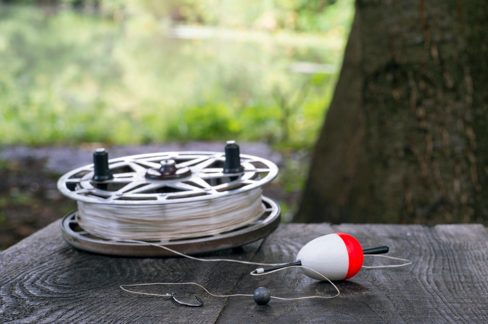 Fishing reel with fishing line, red and white float, hook and sinker on wooden table on natural background. The concept of classic fishing tackle. Text space.