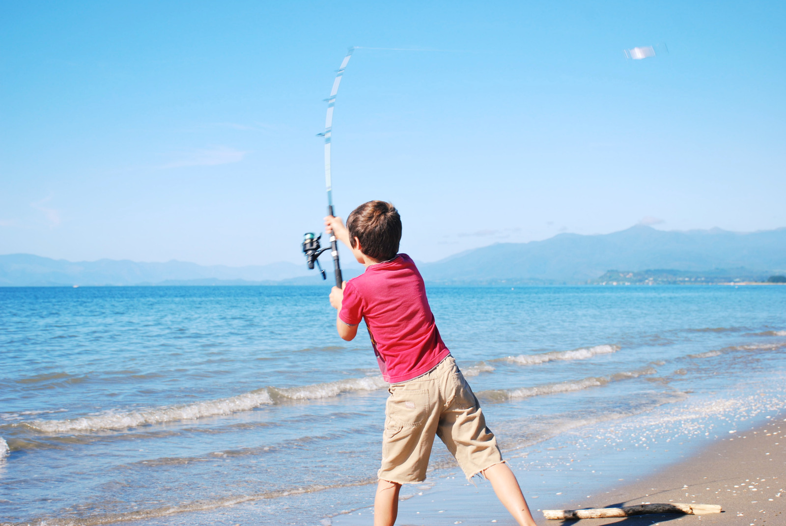 A boy child fishes with his rod against a seascape background on a surf fishing trip in summer.